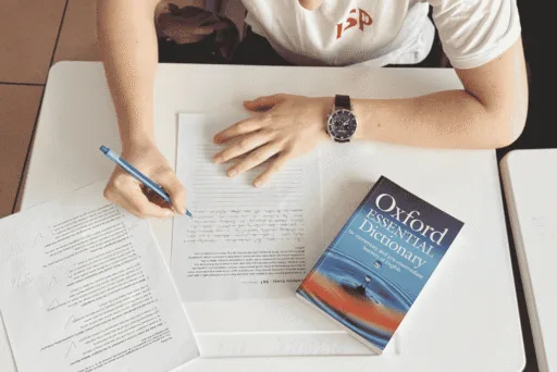 A person sitting at a table writing on paper with a pen.