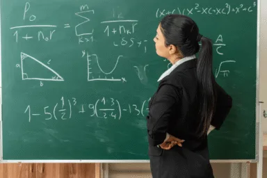 Person in a business suit standing in front of a blackboard.