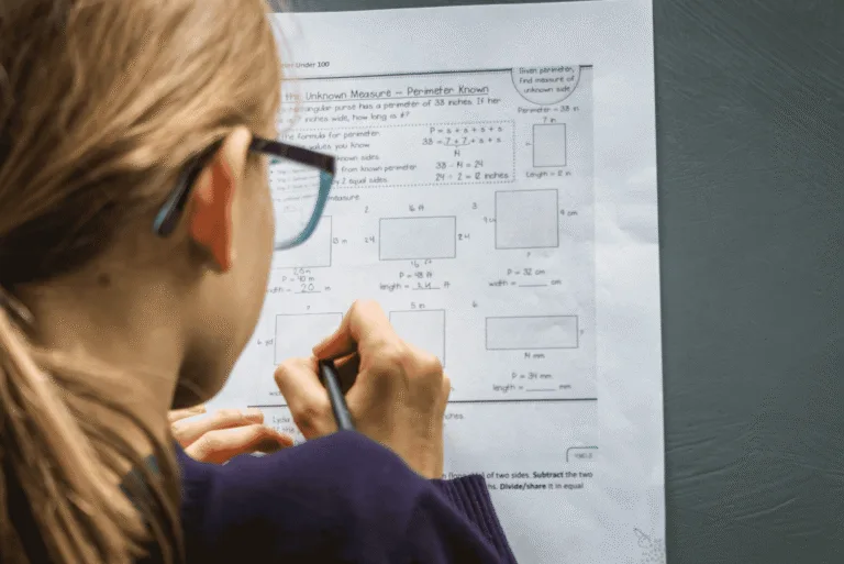 A person wearing glasses writing on a sheet of paper.
